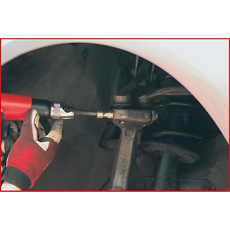 Eine Hand hält einen roten Schlagschrauber, der an einem Fahrzeug montiert wird. Handschuh, silberne Metallteile sichtbar.